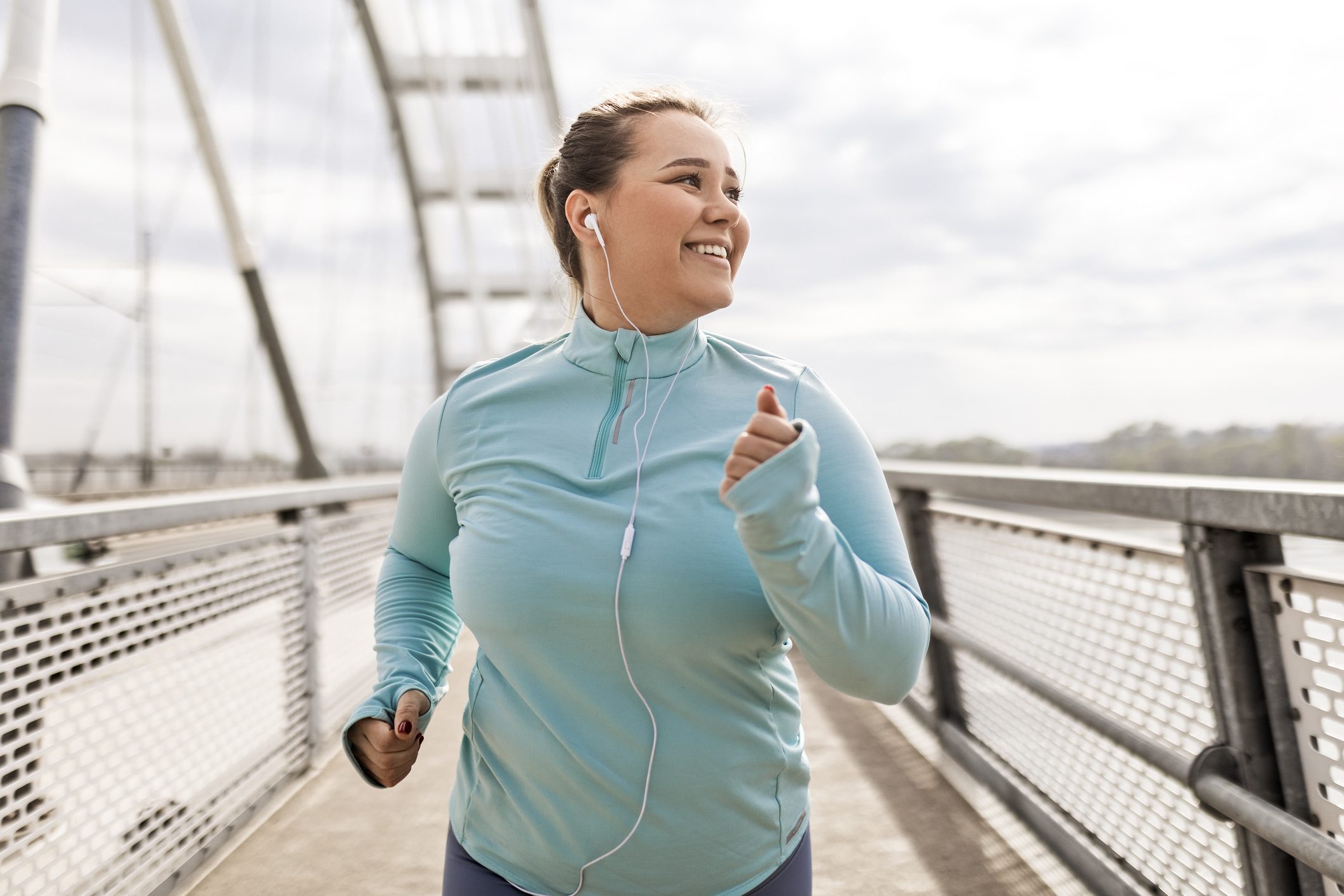 Woman jogging with earphones on bridge.