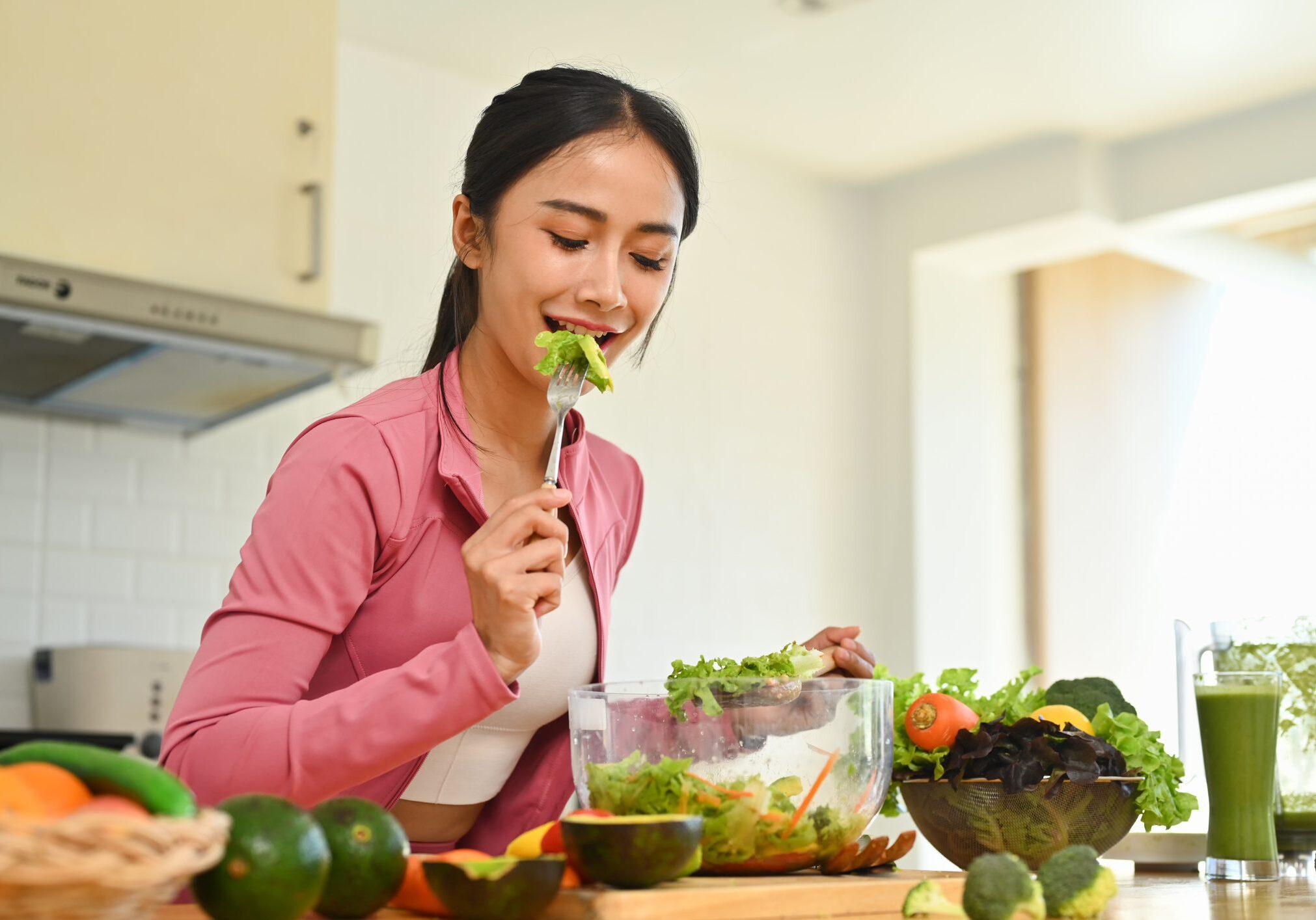 Woman eating salad in a kitchen.