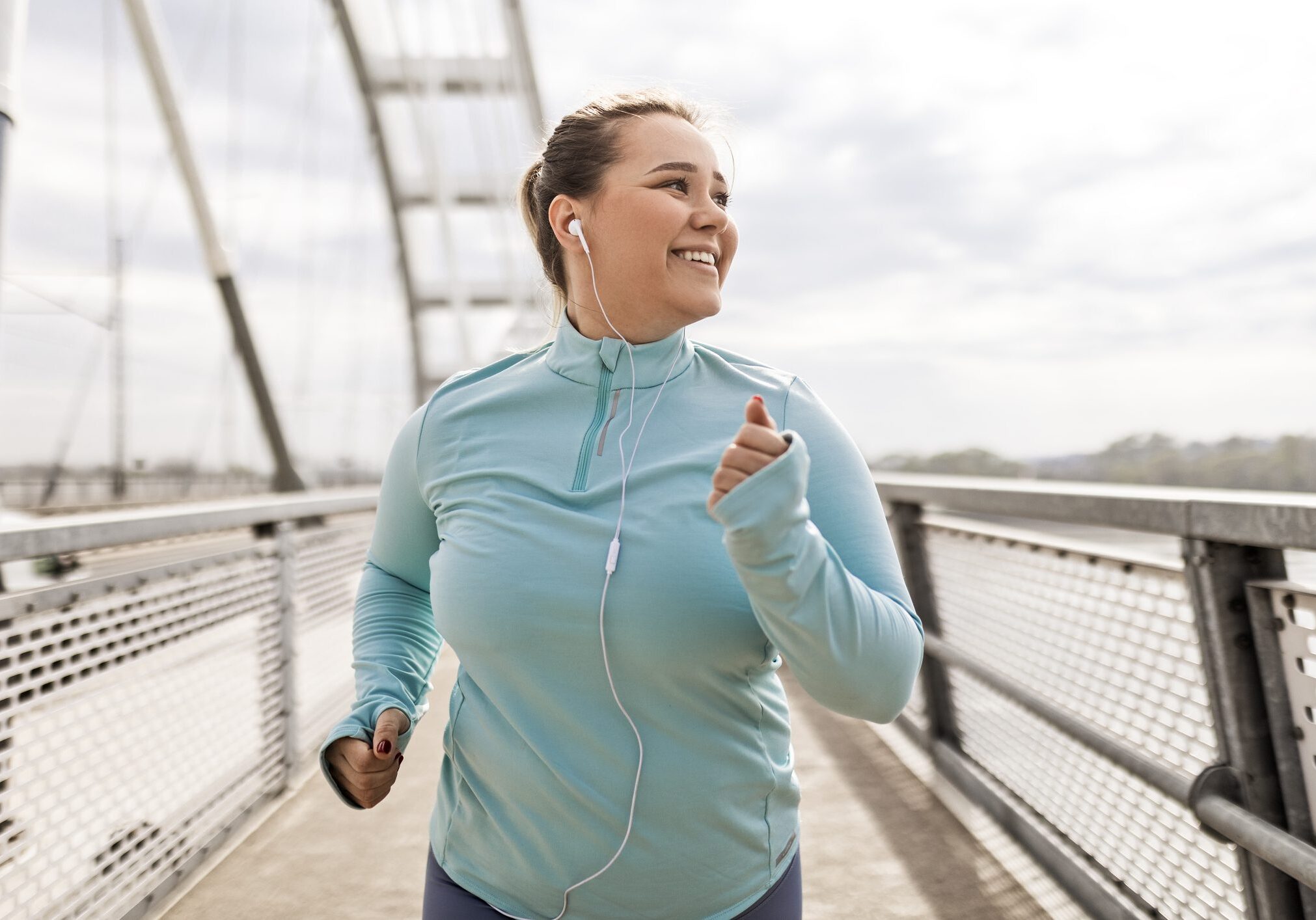Woman jogging with earphones on bridge.